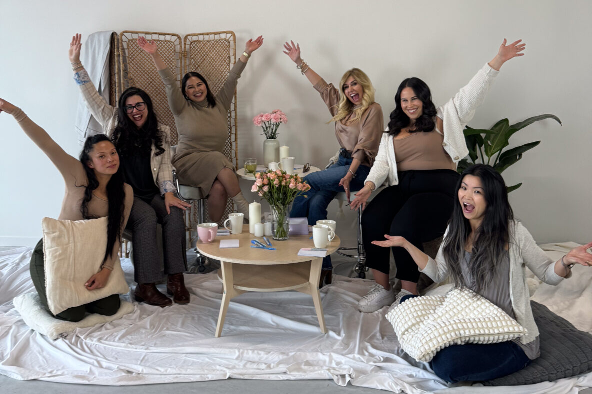 Six women gathered for a group discussion smiling and waving