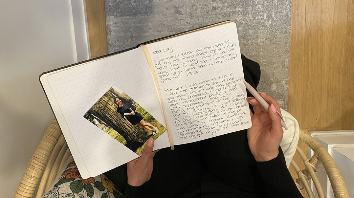Marjan sitting on a chair and looking at the letter she wrote herself with a picture of her younger self.