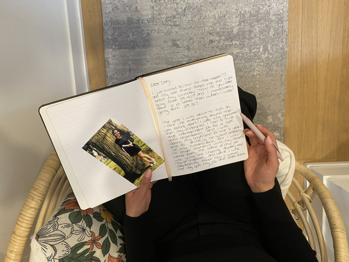 Marjan sitting on a chair and looking at the letter she wrote herself with a picture of her younger self.